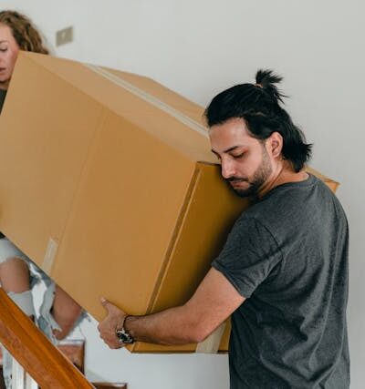 Concentrated couple carrying big carton box down stairs