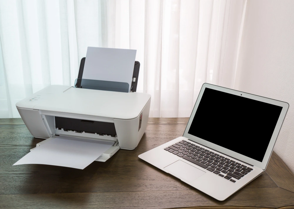 Laptop on a wooden table with a printer