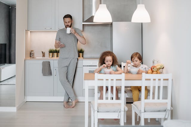 A Man Standing Beside His Kids while Using His Mobile Phone