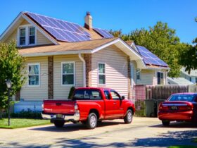 The house has solar panels on its roof and a car is parked in front of the house