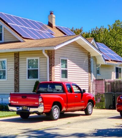 The house has solar panels on its roof and a car is parked in front of the house